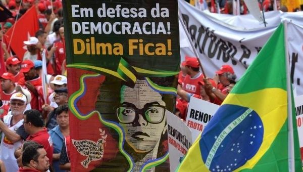 A photo from a March 13, 2015 rally in Sao Paulo features a poster with an image of a young Dilma Rousseff that reads, “In defense of democracy, Dilma stays!”