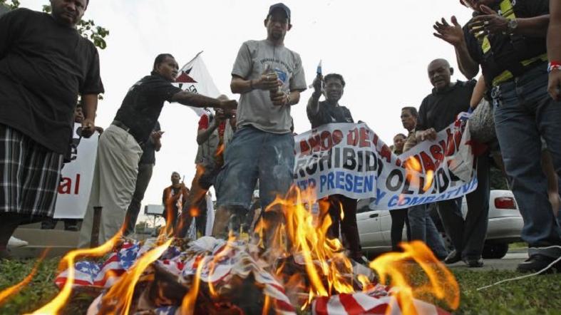 Protesters gather around a burning U.S. flag during a march marking the 25th anniversary of the U.S invasion of Panama in Panama City, Dec. 20, 2014.