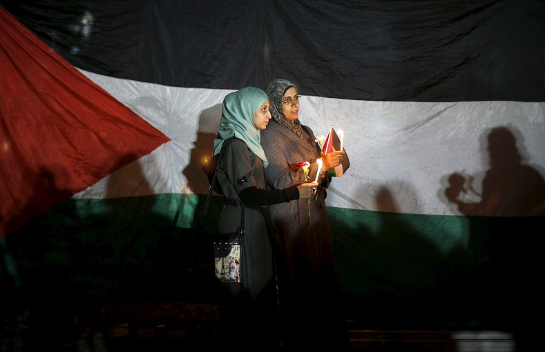 Women hold candles as they stand in front of a Palestinian flag during a rally to pay tribute to Palestinians killed by Israeli troops.