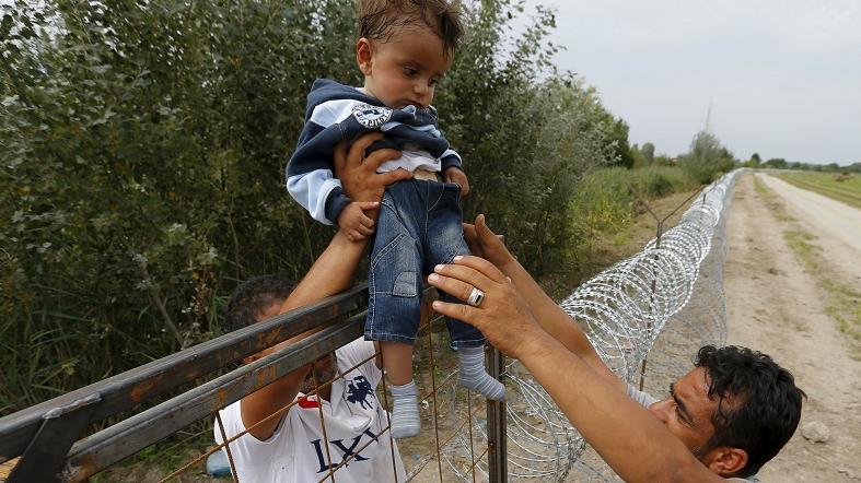 A Syrian refugee lifts a child over a fence on the Hungarian-Serbian border near Asotthalom, Hungary, Aug. 25, 2015.