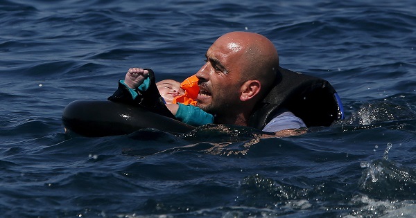 A Syrian refugee holding a baby swims toward the shore after their dinghy deflated some 100 meters off the Greek island of Lesbos on Sept. 13, 2015.
