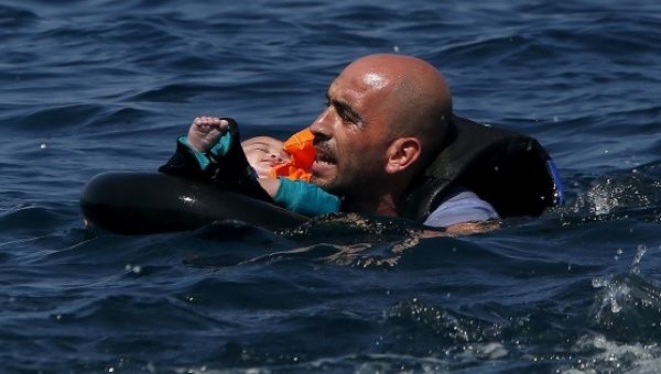 A Syrian refugee holding a baby swims toward the shore after their dinghy deflated some 100 meters off the Greek island of Lesbos on Sept. 13, 2015.