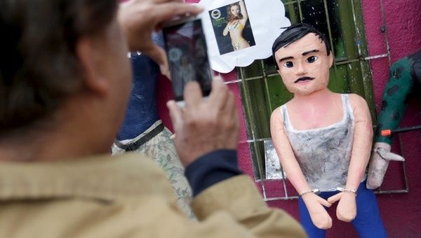 A pedestrian takes a photo with his cellphone of a pinata depicting the drug lord Joaquin 