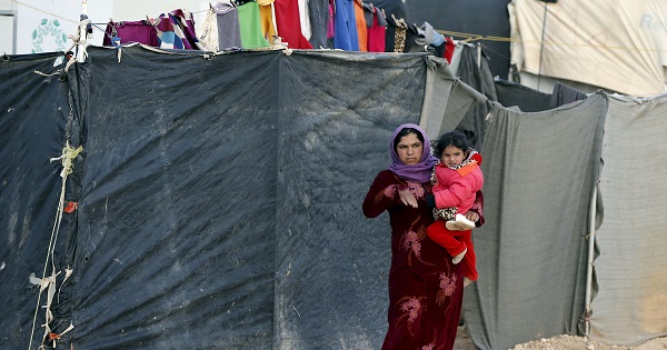 A Syrian refugee woman carrying her child looks at the convoy of U.N. High Commissioner for Refugees, January 18, 2016.