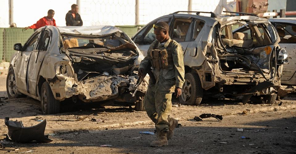 A Somali soldier walks past wrecked cars in front of the Lido Seafood restaurant in Mogadishu on Jan. 22, 2016 following an overnight attack