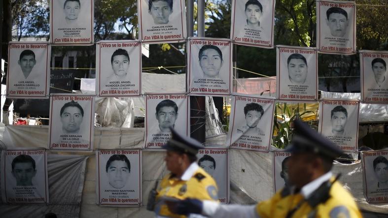 Police stand in front of pictures of the 43 missing Ayotzinapa students as their relatives take part in a meeting with Attorney General Arely Gomez, Jan. 14, 2016.