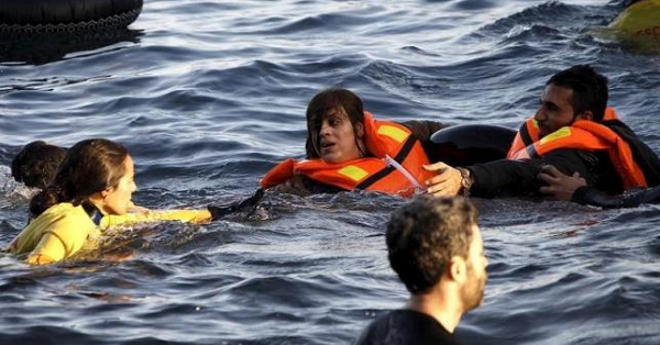 A volunteer lifeguard (L) helps a refugee as a boat carrying around 150 refugees arrives after crossing part of the Aegean sea from Turkey on the Greek island of Lesbos, Oct. 30, 2015.