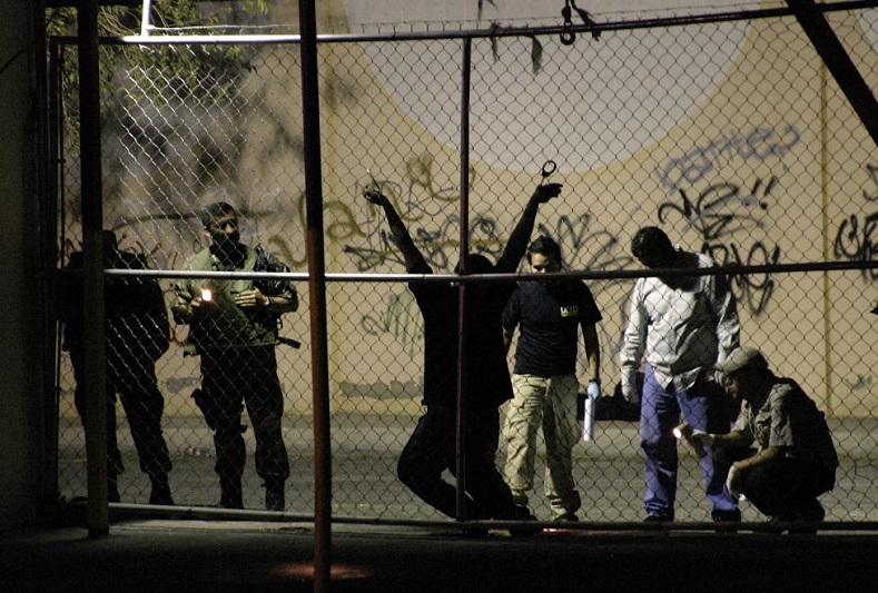 Military and forensic experts inspect the body of a man who was killed outside a nightclub in the border city of Ciudad Juarez August 31, 2009. A man was handcuffed to a fence and shot several times by drug hit men outside a nightclub, according to local media. 