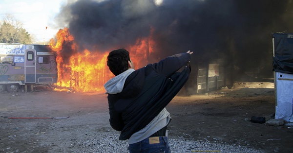 A youth throws a stone as flames rise from a burning makeshift shelter in protest against the dismantlement of the 