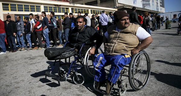 A Syrian and an Iraqi refugee, both on wheelchairs, wait for a food distribution as refugees and migrants line up outside a passenger terminal used as shelter at the port of Piraeus, near Athens.