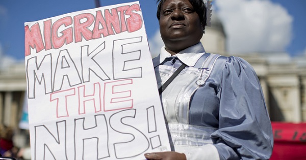 A protester holds a sign highlighting that many migrants work in Britain's National Health System. Many who work in the NHS would not make the new threshold.