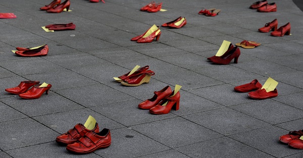 A man stands next to red shoes used for a performance to denounce violence against women organized by Amnesty International during International Women's Day in Gijon.