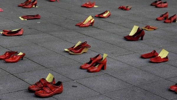 A man stands next to red shoes used for a performance to denounce violence against women organized by Amnesty International during International Women's Day in Gijon.