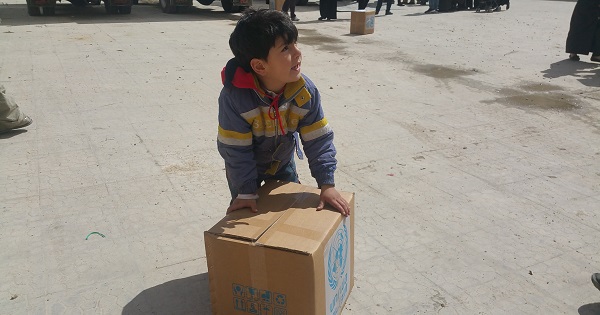 A boy stands next to a U.N. aid parcel.