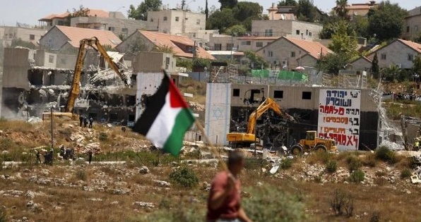 A Palestinian flag as Israeli heavy machinery demolish apartment blocs in the West Bank Jewish settlement of Beit El July 29, 2015.