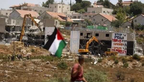A Palestinian flag as Israeli heavy machinery demolish apartment blocs in the West Bank Jewish settlement of Beit El July 29, 2015. 