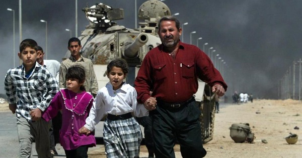 A family flees past a destroyed Iraqi T-55 tank after a mortar attack on British Army positions in the southern city of Basra, March 28, 2003.