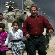 A family flees past a destroyed Iraqi T-55 tank after a mortar attack on British Army positions in the southern city of Basra, March 28, 2003.