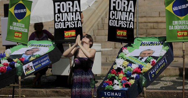 A protester kneels with mock coffins of house speaker Eduardo Cunha and Vice President Michel Temer with 