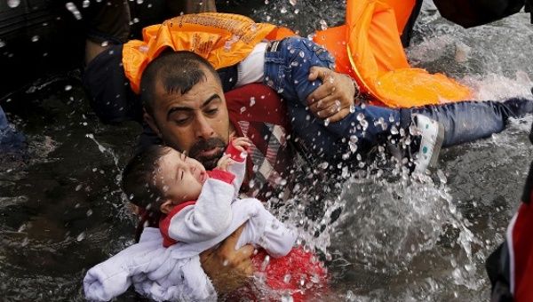 A Syrian man holds onto his children as he struggles the Greek island of Lesbos, after crossing a part of the Aegean Sea from Turkey to Lesbos Sept. 24, 2015.