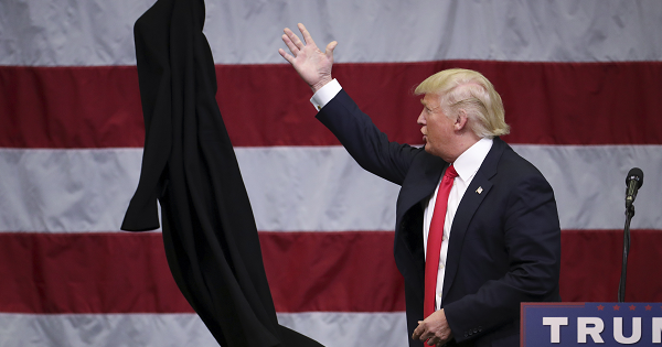 Donald Trump tosses off his overcoat as he speaks at a campaign event in an airplane hangar in Rome, New York, April 12, 2016.