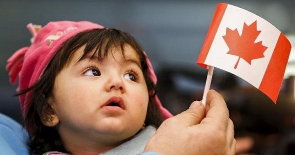 A young Syrian refugee looks up as her father holds her and a Canadian flag at the as they arrive at Pearson Toronto International Airport in Mississauga, Ontario, December 18, 2015.