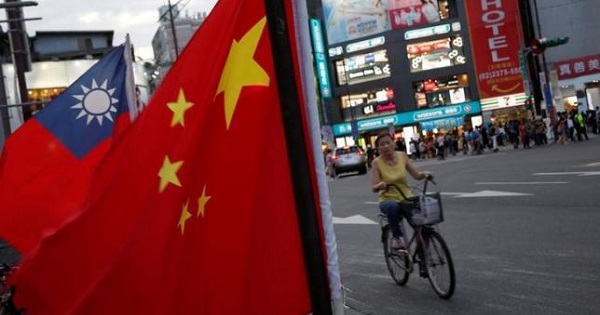 A woman rides a bike past Taiwan and China national flags during a rally held by a group of pro-China supporters calling for peaceful reunification, Taipei, May 14, 2016.