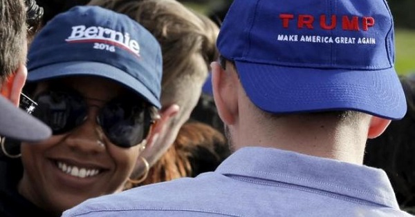 A woman wearing a hat with the word 'Bernie' smiles towards a man wearing a hat stating 'Trump' at a Sanders rally in New York March 31, 2016.