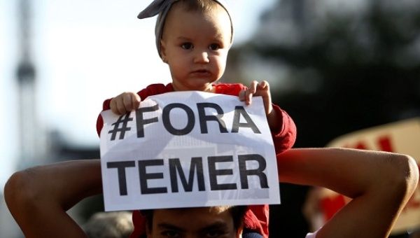 An infant holds a sign reading 