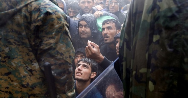 Refugees beg Macedonian policemen to let them cross the border from Greece into Macedonia during a rainstorm, Sept.10, 2015.