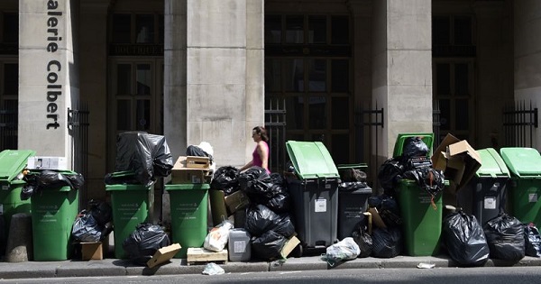 Pedestrians walk past trash piling up on the pavement of rue Des Petits Champs in central Paris on June 8, 2016.