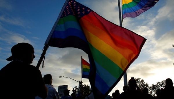 Mourners gather under an LGBT pride flag flying at half-mast for a candlelight vigil in remembrance for Orlando victims, from San Diego, California, U.S. June 12, 2016.