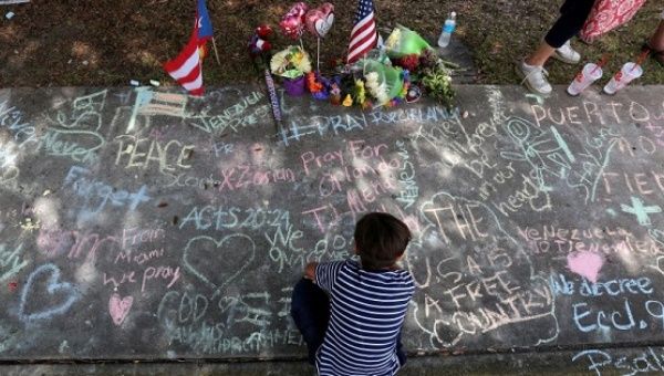 A child draws on the sidewalk in chalk at a makeshift memorial that is across the street from Pulse night club following last week's shooting in Orlando, Florida.