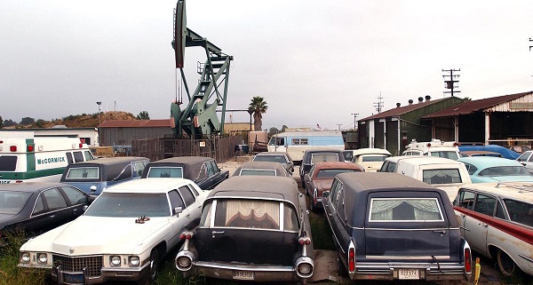 An oil well pumps next to yard containing junked hearses and ambulances near Signal Hill in Long Beach, California, on May 29, 2003.