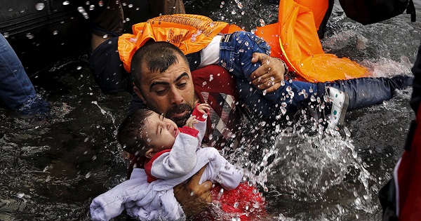 A Syrian refugee holds onto his children as he struggles to get off a dinghy on the Greek island of Lesbos, after crossing from Turkey.
