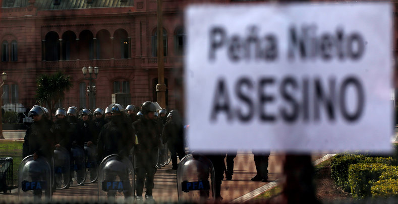 Argentine policemen stand behind a fence with a sign placed on it that reads 