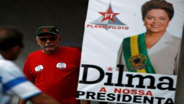 People walk next to an official photo of Brazil's suspended President Dilma Rousseff, at a camp in support of Rousseff, in Brasilia, Brazil, August 28, 2016. 
