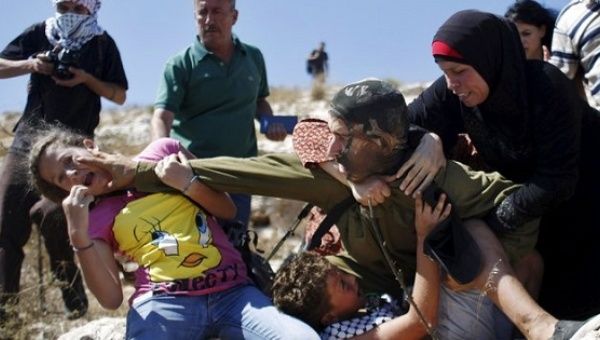 Palestinian protesters struggle with an Israeli soldier to prevent the arrest of a boy for throwing rocks.