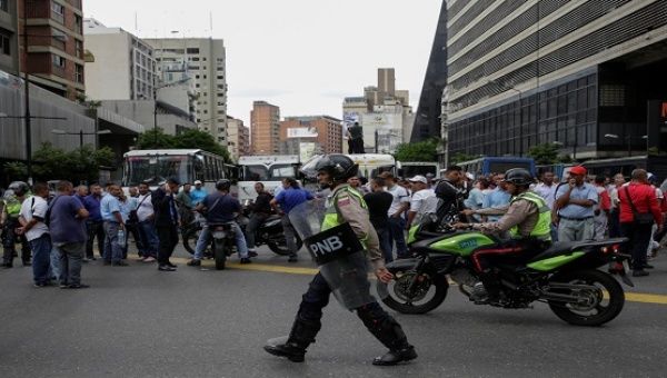 A riot police officer walks past demonstrators during a public transport protest in Caracas, Venezuela September 21, 2016.