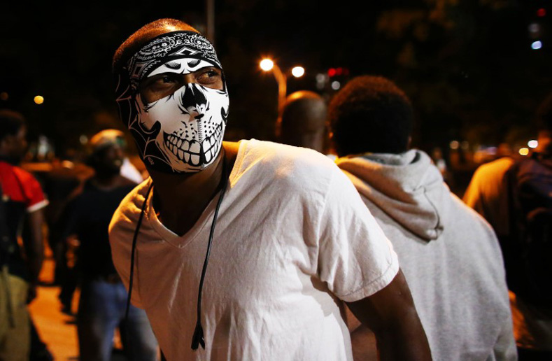 A masked protester walks in the streets downtown during another night of protests over the police shooting of Keith Scott in Charlotte, North Carolina Sept. 22, 2016. 