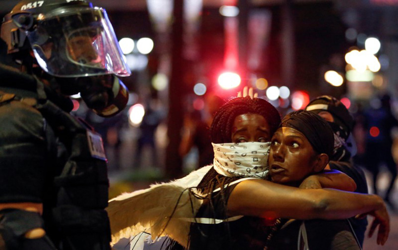 Two women embrace while looking at a police officer in uptown Charlotte, NC during a protest of the police shooting of Keith Scott, in Charlotte, North Carolina, Sept. 21, 2016. 
