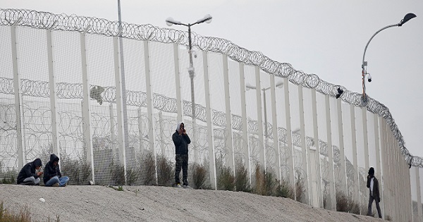 Migrants are seen near the razor-wire topped fence in Calais, France, which secures the road approach to the city and dissuade them from trying to reach Britain on lorries.
