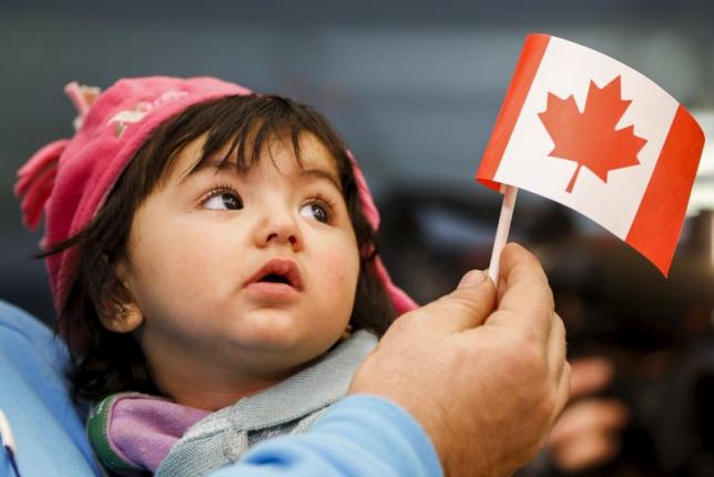 A young Syrian refugee looks up as her father holds her and a Canadian flag at Pearson Toronto International Airport in Mississauga, Ontario, Dec. 18, 2015.