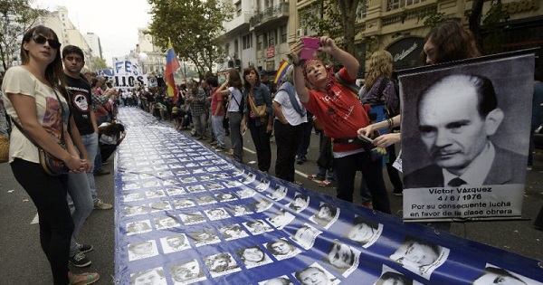Demonstrators surround a large banner with portraits of people disappeared in the 1976-1983 military dictatorship during a gathering to commemorate the anniversary of the coup of 1976, at Plaza de Mayo Square in Buenos Aires on March 24, 2015.