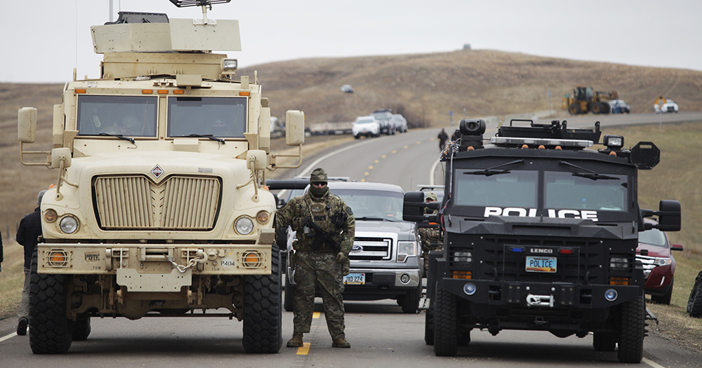 A North Dakota police officer stands next to two armored vehicles just beyond the police barricade on Highway 1806 near a DAPL construction site.