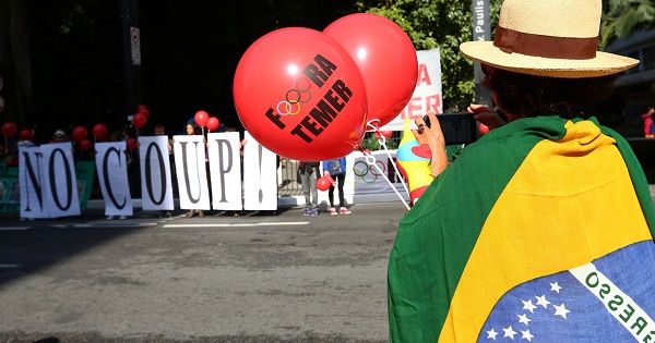 A demonstrator wearing a Brazilian flag carries a balloon reading 