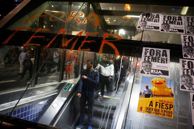 People go down the escalator in front of a phrase and posters with the image Brazil's interim President Michel Temer at the entrance of a subway, after the Brazilian Senate voted to impeach President Dilma Rousseff, at Paulista Avenue in Sao Paulo, Brazil, May 12, 2016. The words read: 