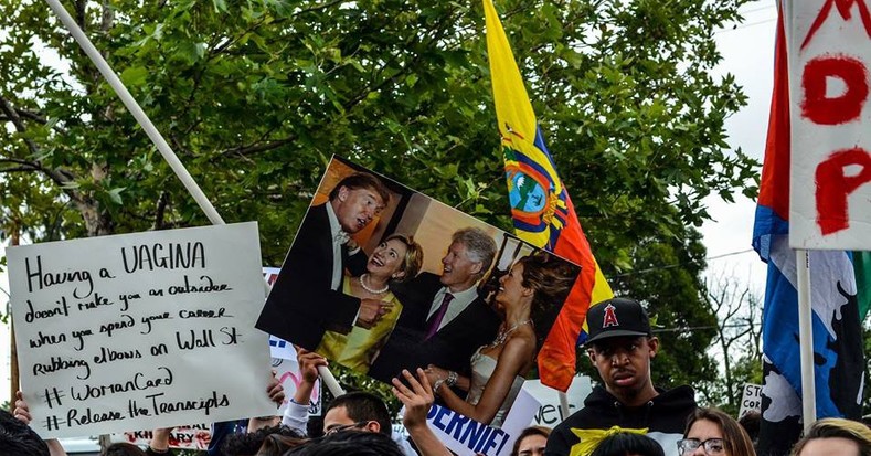 Protesters at East Los Angeles College hold signs depicting the Clintons socializing with presumptive Republican presidential candidate Donald Trump, May 5, 2016