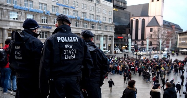 Police look on as refugees demonstrate against violence near the main Cologne train station.