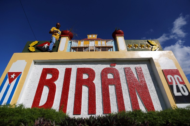 A man stands on top of a sign with a model of the house where Cuba's former President Fidel Castro was born, in Biran.